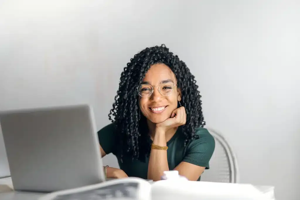 pexels photo 3769021 3769021 Joyful businesswoman with curly hair smiling at camera while using laptop indoors.