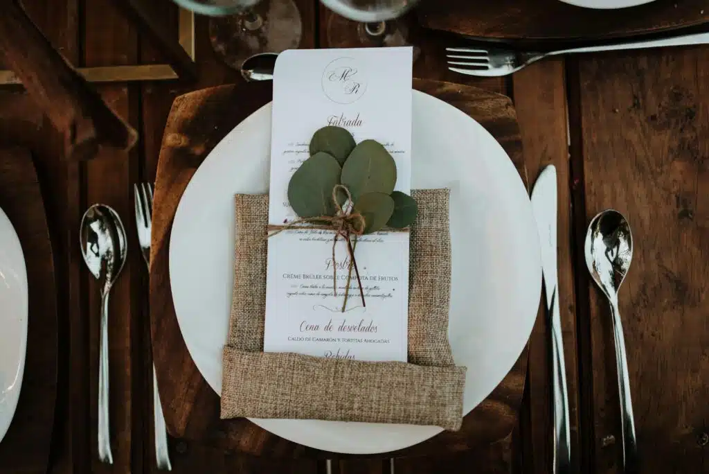 pexels photo 11655012 11655012 Stylish table setup featuring a menu card with eucalyptus leaves on a rustic wooden table.